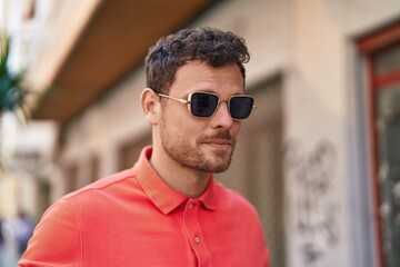 Young hispanic man with relaxed expression wearing sunglasses at street