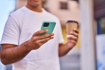 Young hispanic man using smartphone drinking coffee at street
