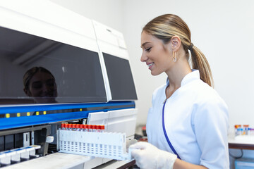 Lab tech loading samples into a chemistry analyzer. female lab tech loading specimen for...