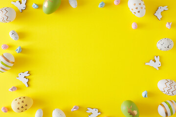 Easter decorations concept. Top view photo of color eggs and cute easter bunnies on yellow background with copyspace in the middle. Holiday invitation card idea.