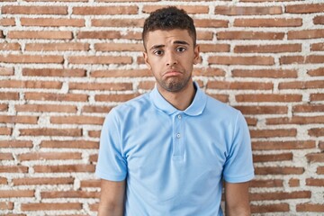Brazilian young man standing over brick wall depressed and worry for distress, crying angry and...