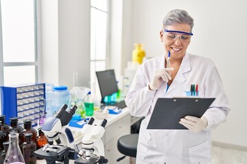 Middle age woman wearing scientist uniform writing on clipboard at laboratory