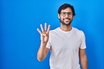 Handsome latin man standing over blue background showing and pointing up with fingers number four while smiling confident and happy.
