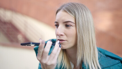 Young blonde woman sending voice message with smartphone at street