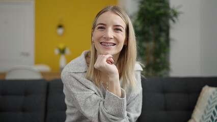 Young blonde woman smiling confident sitting on the sofa at home
