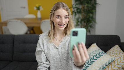 Fototapeta na wymiar Young blonde woman taking selfie picture with smartphone sitting on the sofa at home