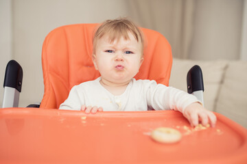 a small child sits in a chair for feeding and is naughty, cries, does not want to eat food.