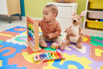 Adorable hispanic toddler playing with abacus sitting on floor at kindergarten