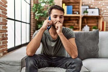 Young hispanic man worried talking on the smartphone at home
