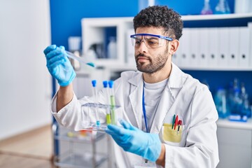 Young arab man wearing scientist uniform holding test tubes at laboratory