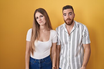 Young couple standing over yellow background looking sleepy and tired, exhausted for fatigue and hangover, lazy eyes in the morning.