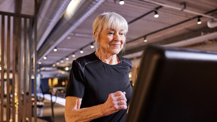 Smiling senior woman exercising on a treadmill, woman running working out in gym
