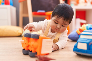 Adorable hispanic baby playing with cars toy lying on floor at kindergarten