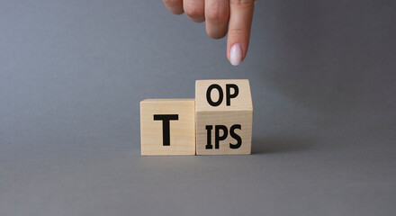 Top Tips symbol. Businessman hand points at turned wooden cubes with words Top Tips. Beautiful grey...