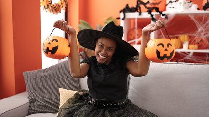African american woman wearing witch costume holding halloween pumpkin baskets at home