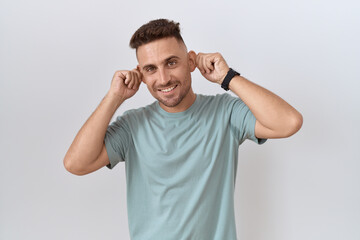 Fototapeta na wymiar Hispanic man with beard standing over white background smiling pulling ears with fingers, funny gesture. audition problem