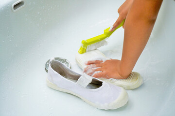 洗面台で自分の上靴の底をブラシで綺麗に磨いて家事を手伝う幼児の手