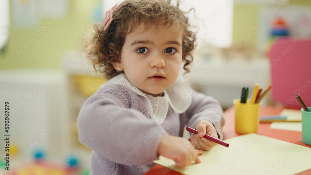 Wall mural Adorable hispanic girl preschool student sitting on table drawing on paper at kindergarten