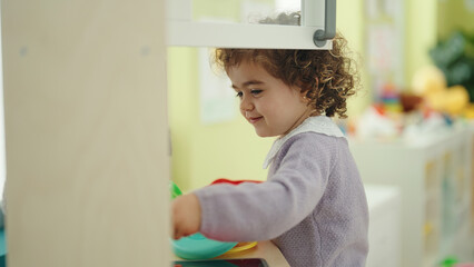 Fototapeta na wymiar Adorable hispanic girl playing with play kitchen standing at kindergarten