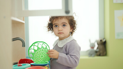 Adorable hispanic girl playing with play kitchen standing at kindergarten