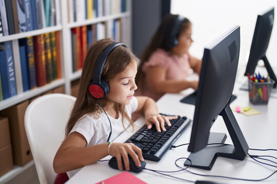 Two kids students wearing headphones using computer studying at classroom