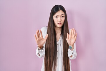 Chinese young woman standing over pink background moving away hands palms showing refusal and denial with afraid and disgusting expression. stop and forbidden.