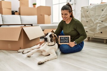 Young woman sitting on floor with dog holding new home blackboard message at home