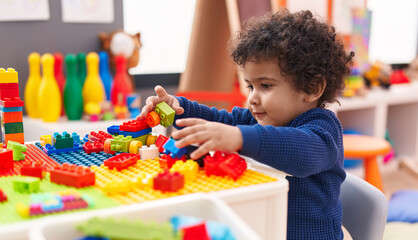 Adorable hispanic toddler playing with construction blocks sitting on table at kindergarten
