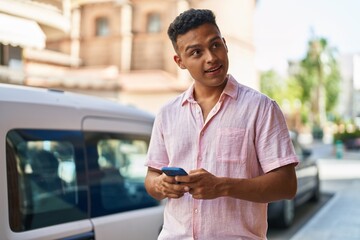 Young latin man smiling confident using smartphone at street