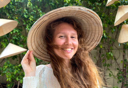 Portrait of happy positive young woman traveler in Vietnamese wicker traditional hat in Asia, Vietnam