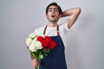 Young hispanic man holding bouquet of white and red roses crazy and scared with hands on head, afraid and surprised of shock with open mouth