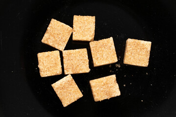 Several cubes of brown sugar on black ceramic, macro, top view.