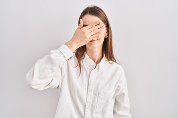 Young caucasian woman standing over isolated background covering eyes with hand, looking serious and sad. sightless, hiding and rejection concept