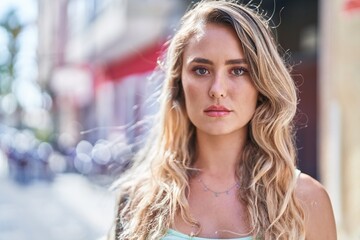 Young blonde woman standing with serious expression at street - obrazy, fototapety, plakaty