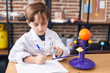 Adorable hispanic boy astronomer student make planetary work writing on notebook at laboratory...