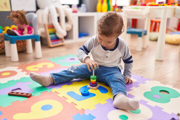 Adorable caucasian boy playing with hoops toy sitting on floor at kindergarten