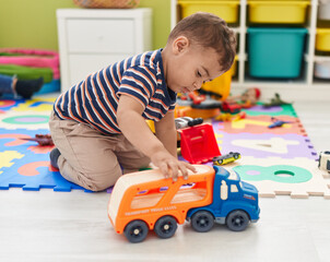 Adorable hispanic toddler playing with cars toy sitting on floor at kindergarten