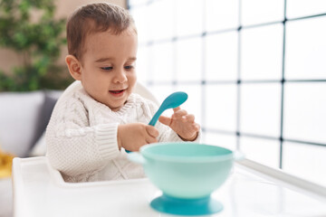 Adorable hispanic toddler smiling confident sitting on highchair at home