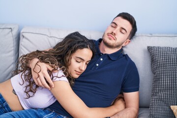 Young hispanic couple hugging each other lying on sofa sleeping at home