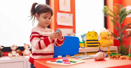 Adorable hispanic girl playing with maths puzzle game standing at kindergarten
