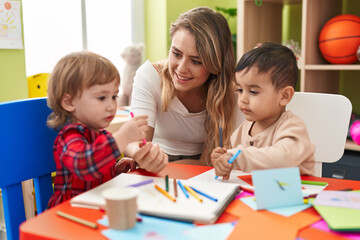Fototapeta premium Teacher with boys sitting on table drawing on paper at kindergarten