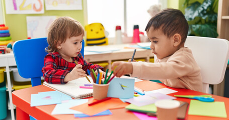 Two kids preschool students sitting on table drawing on paper at kindergarten
