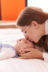 Mother and son lying on bed kissing baby at bedroom