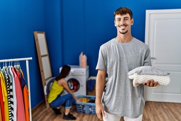 Obraz premium Young handsome man holding folded laundry looking positive and happy standing and smiling with a confident smile showing teeth