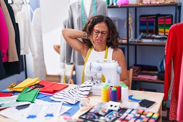 Fototapeta premium Middle age woman tailor stressed using sewing machine at clothing factory