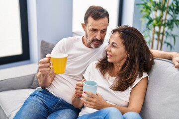 Middle age man and woman couple drinking coffee sitting on sofa at home