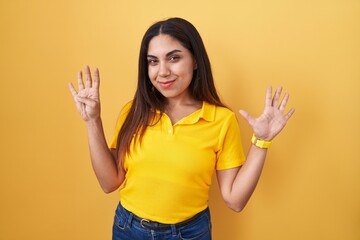 Young arab woman standing over yellow background showing and pointing up with fingers number nine...