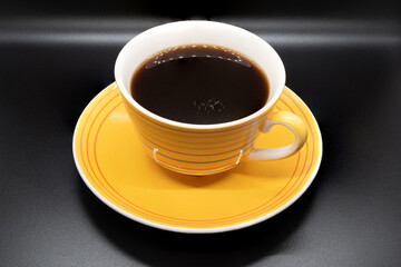 Yellow striped coffee cup and saucer isolated on a black  background