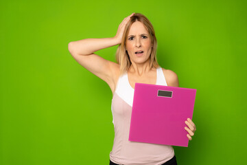 An athlete female holding a weight scale isolated on green background