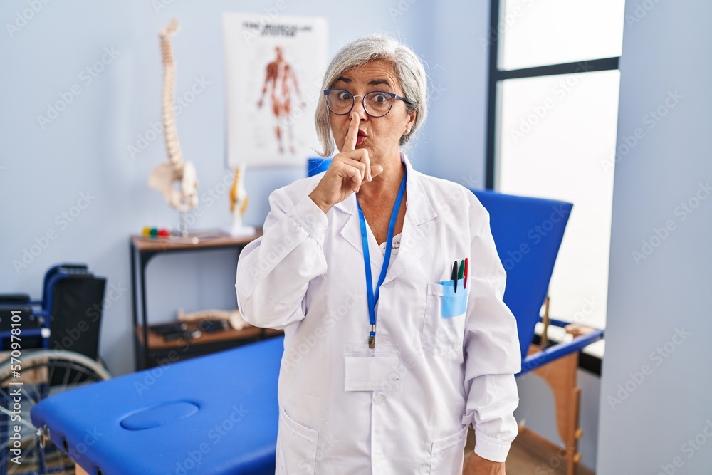 Sticker middle age woman with grey hair working at pain recovery clinic asking to be quiet with finger on li